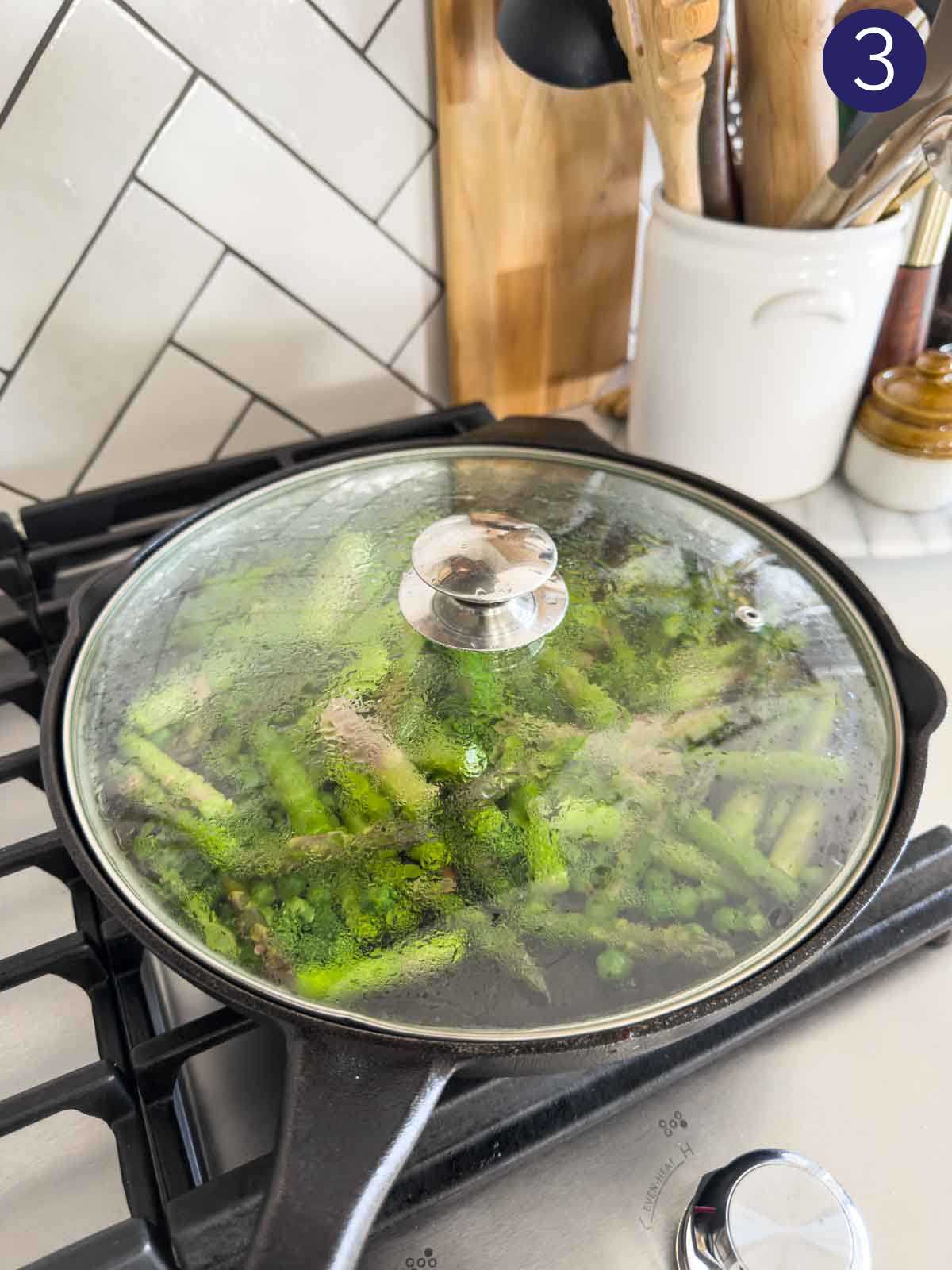Cooking green peas and asparagus in a cast iron pan covered with a glass lid.