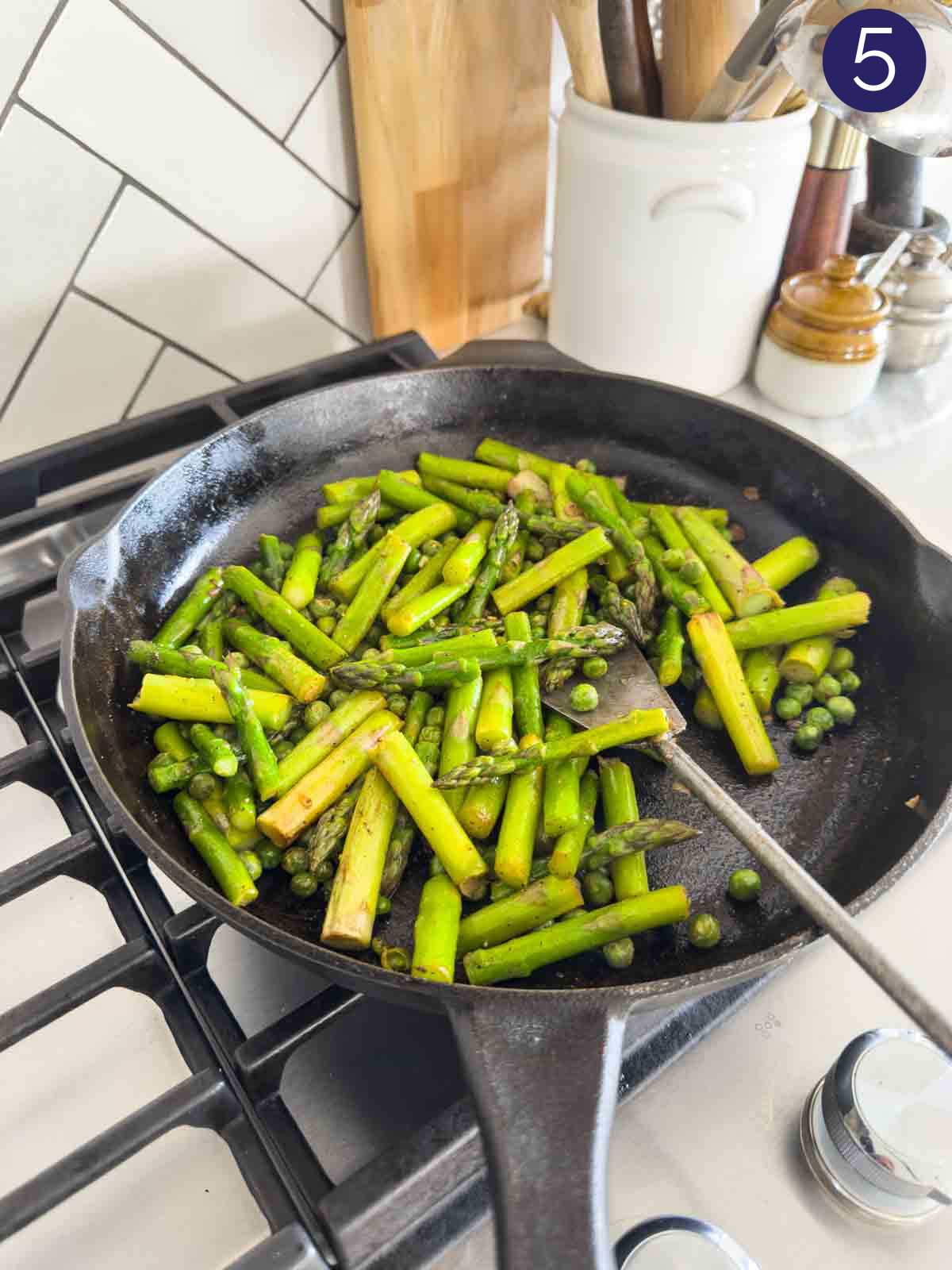 Roasted asparagus and peas in a cast iron pan with a metal spatula.