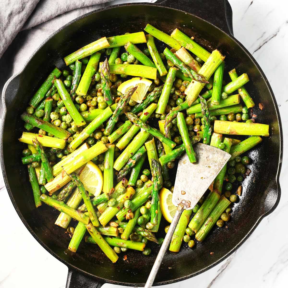 Roasted asparagus and peas in a cast iron pan with a metal spatula.