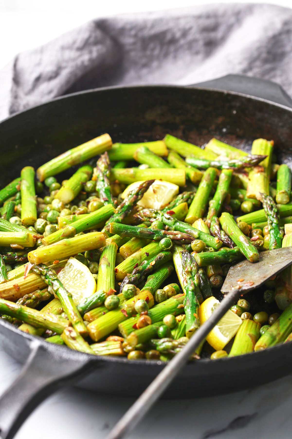 Roasted asparagus and peas in a cast iron pan with a metal spatula.