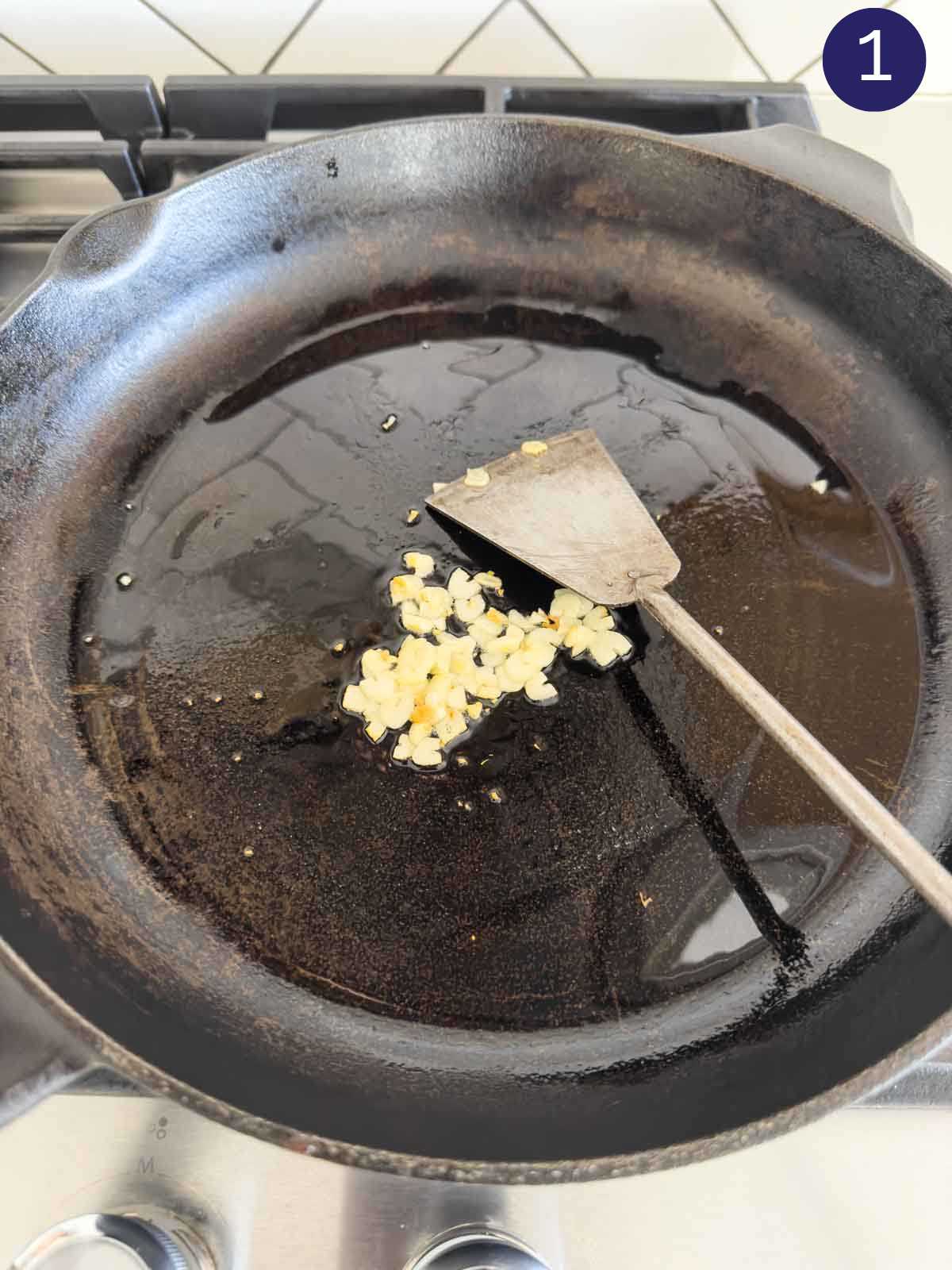 Sautéing garlic in a cast iron pan with a metal spatula.