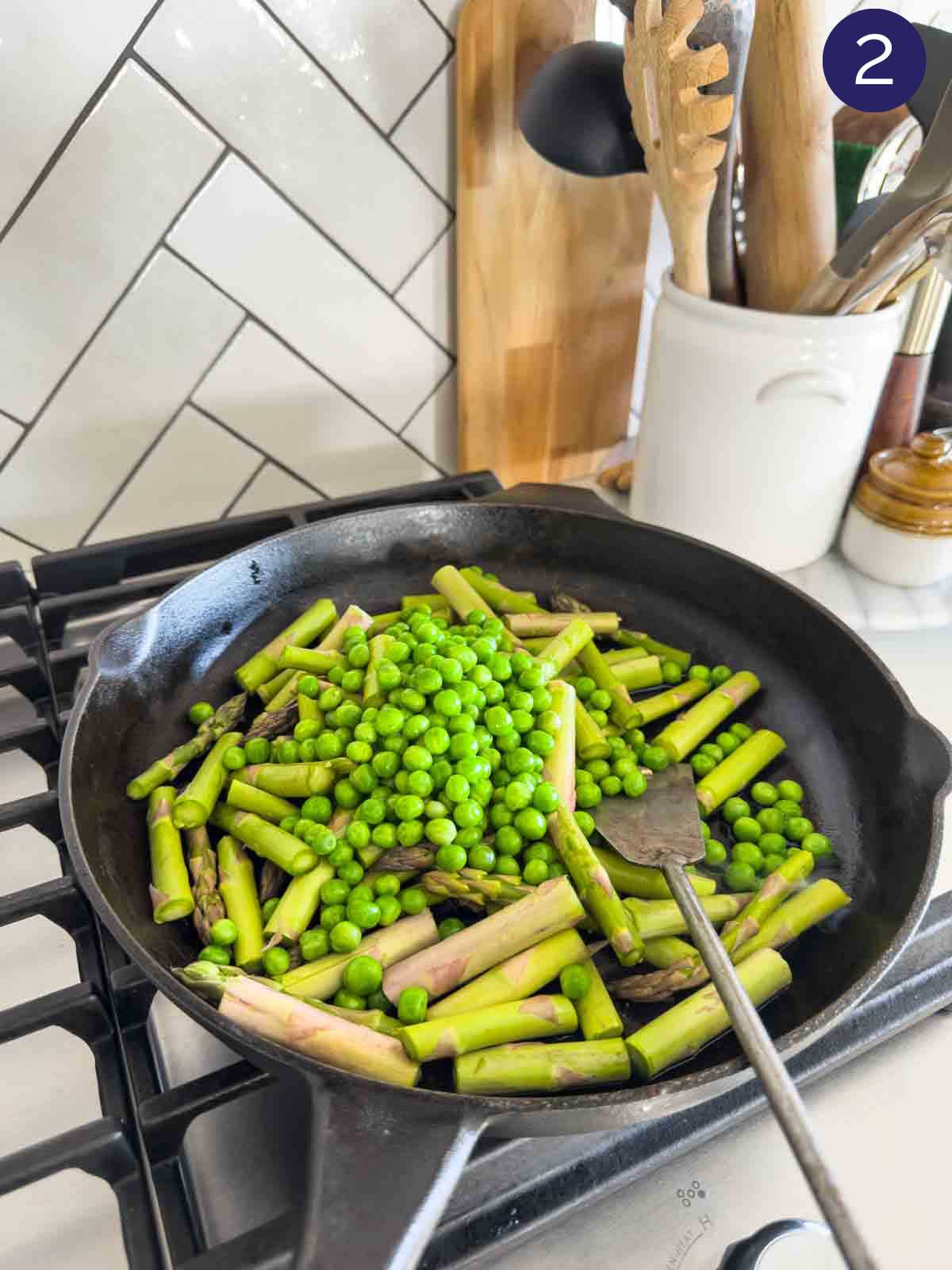 Sautéing green peas and asparagus in a cast iron pan with a metal spatula.