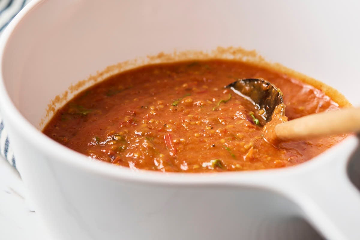 Cherry tomato sauce in a white ceramic saucepan with a wooden spatula after blending.