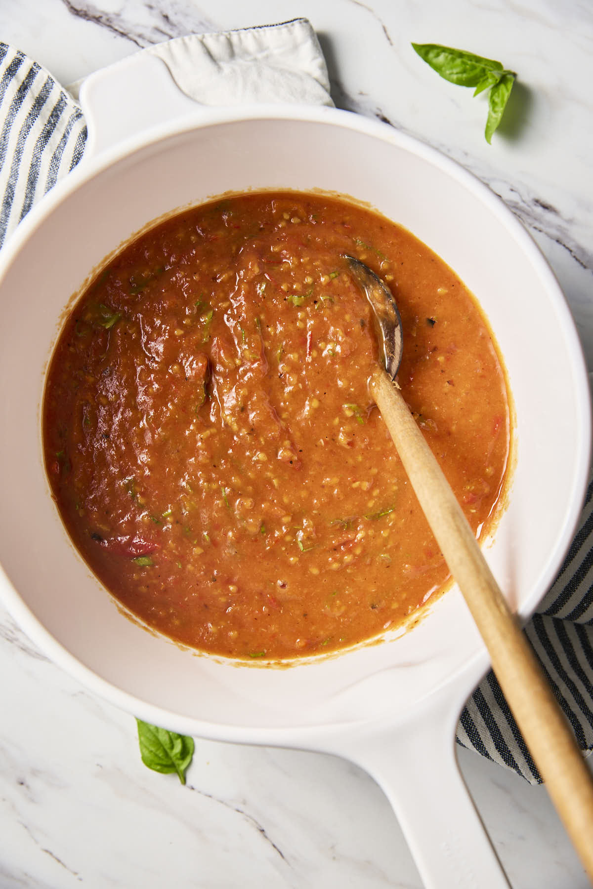 Cherry tomato sauce in a white ceramic saucepan with a wooden spatula.