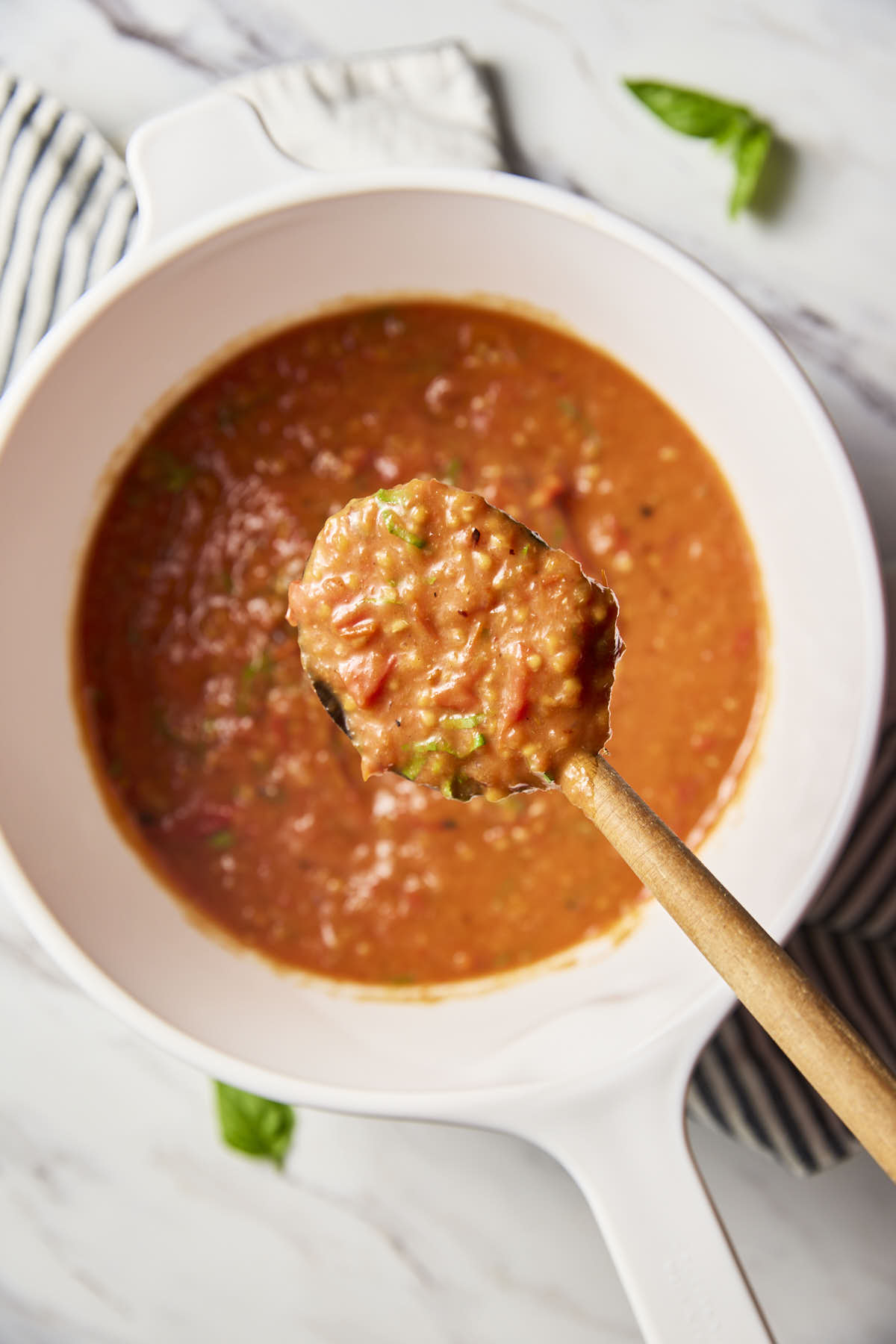 Cherry tomato sauce in a white ceramic saucepan with wooden spatula.
