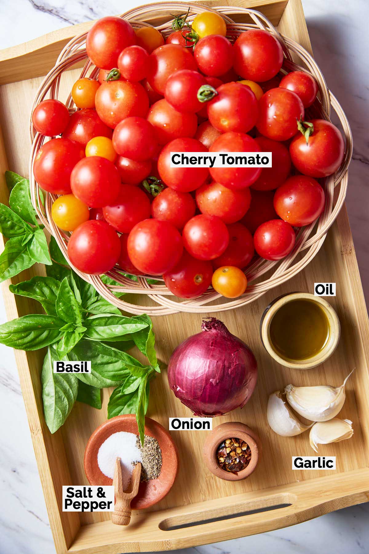 Cherry tomatoes, fresh basil, onion, garlic, chili flakes, olive oil, and salt & pepper arranged on a wooden tray as raw ingredients for preparing the roasted tomato sauce.