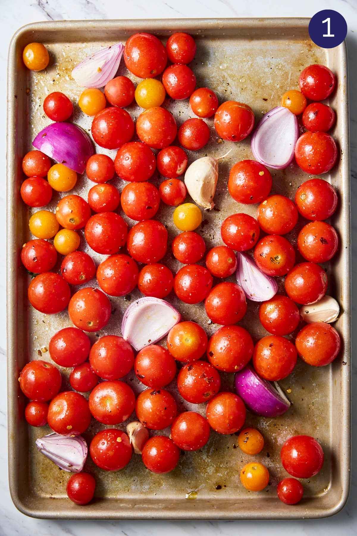 Cherry tomatoes with onion, garlic cloves and seasonings spread on baking sheet to prepare roasted tomato sauce.