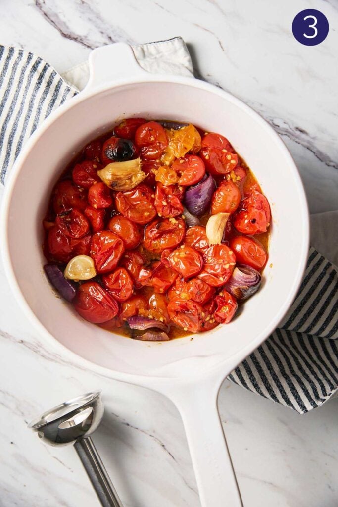 Roasted cherry tomatoes with onion and garlic placed in a white ceramic bowl.