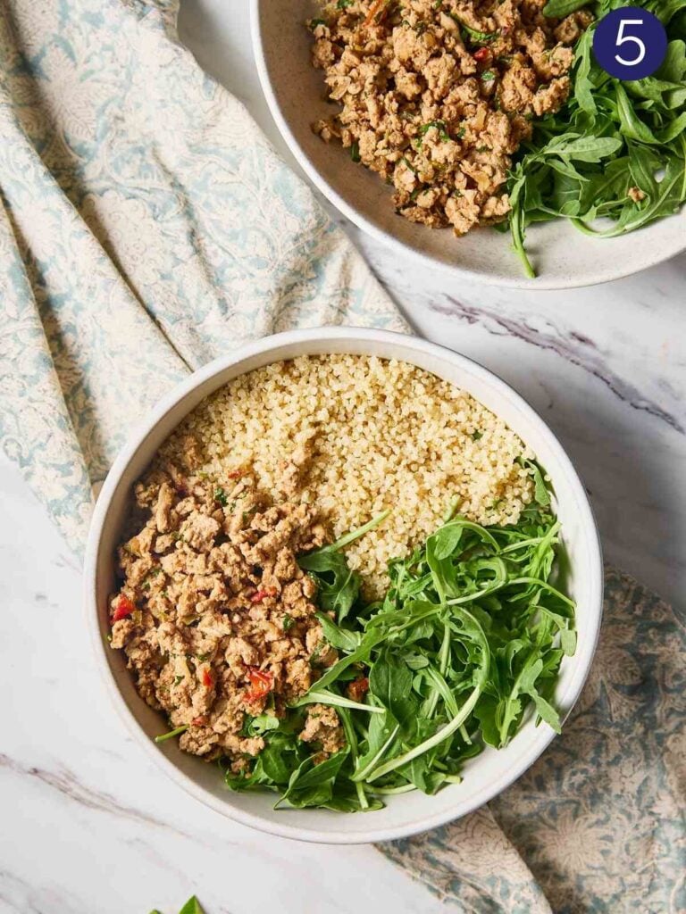 Cooked quinoa, fresh arugula and cooked ground turkey arranged in a serving bowl.