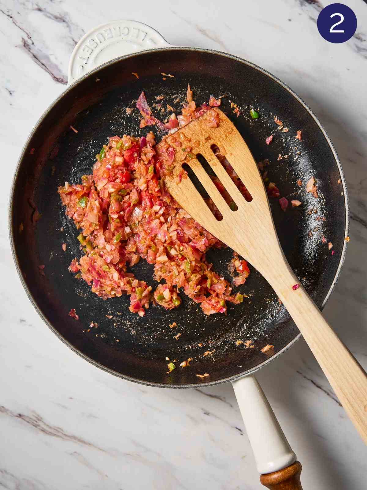 Cooked onion, tomato, garlic and jalapeno mixture in a hot pan with wooden spatula.