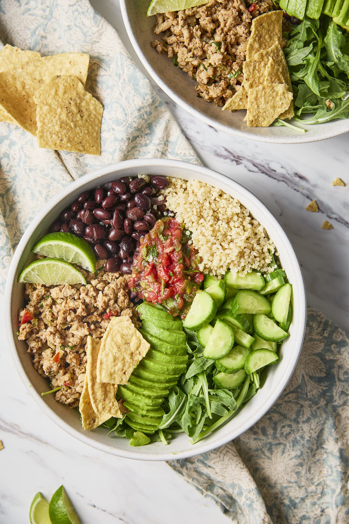Ground turkey, beans, greens and quinoa topped with fresh cucumber, avocado and salsa in a serving bowl to serve as a burrito bowl.
