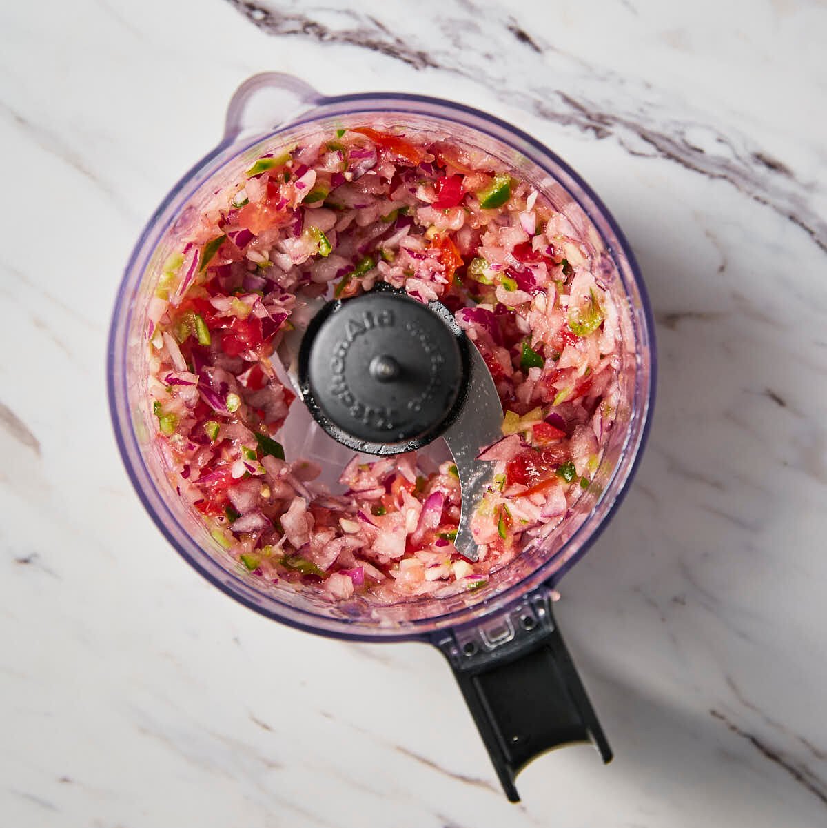 Chopped onion, tomato, garlic and jalapeno mixture in a food processor jar.