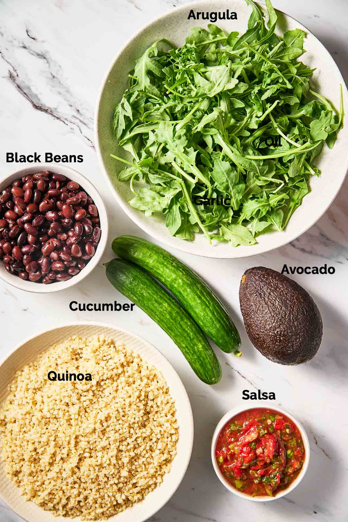 Fresh arugula, black beans, cooked quinoa and salsa, cucumber and avocado placed on a flat surface for making ground turkey burrito bowl.