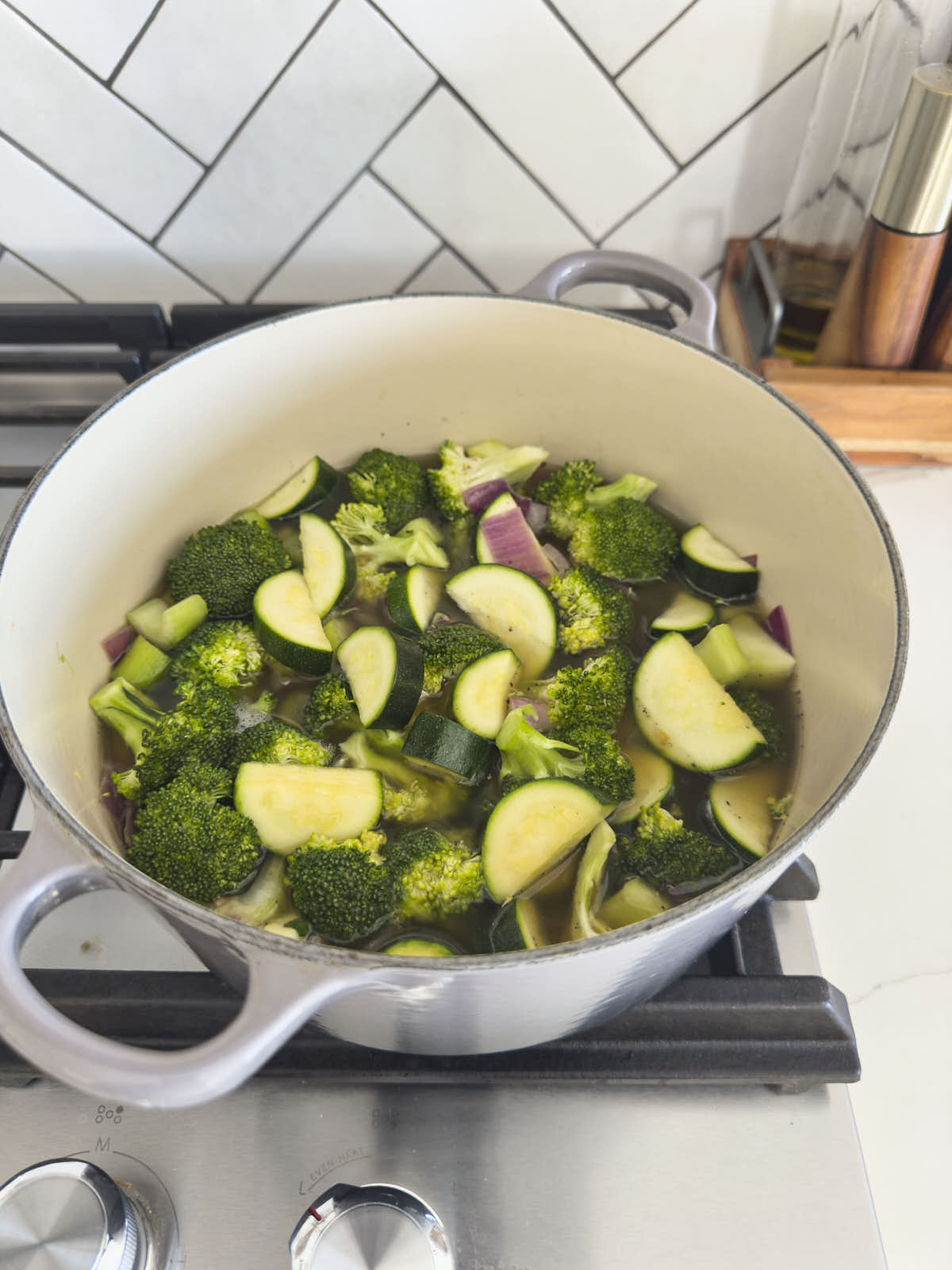 Mixture of broccoli, zucchini. onion and celery with broth in a cast iron pot before cooking.