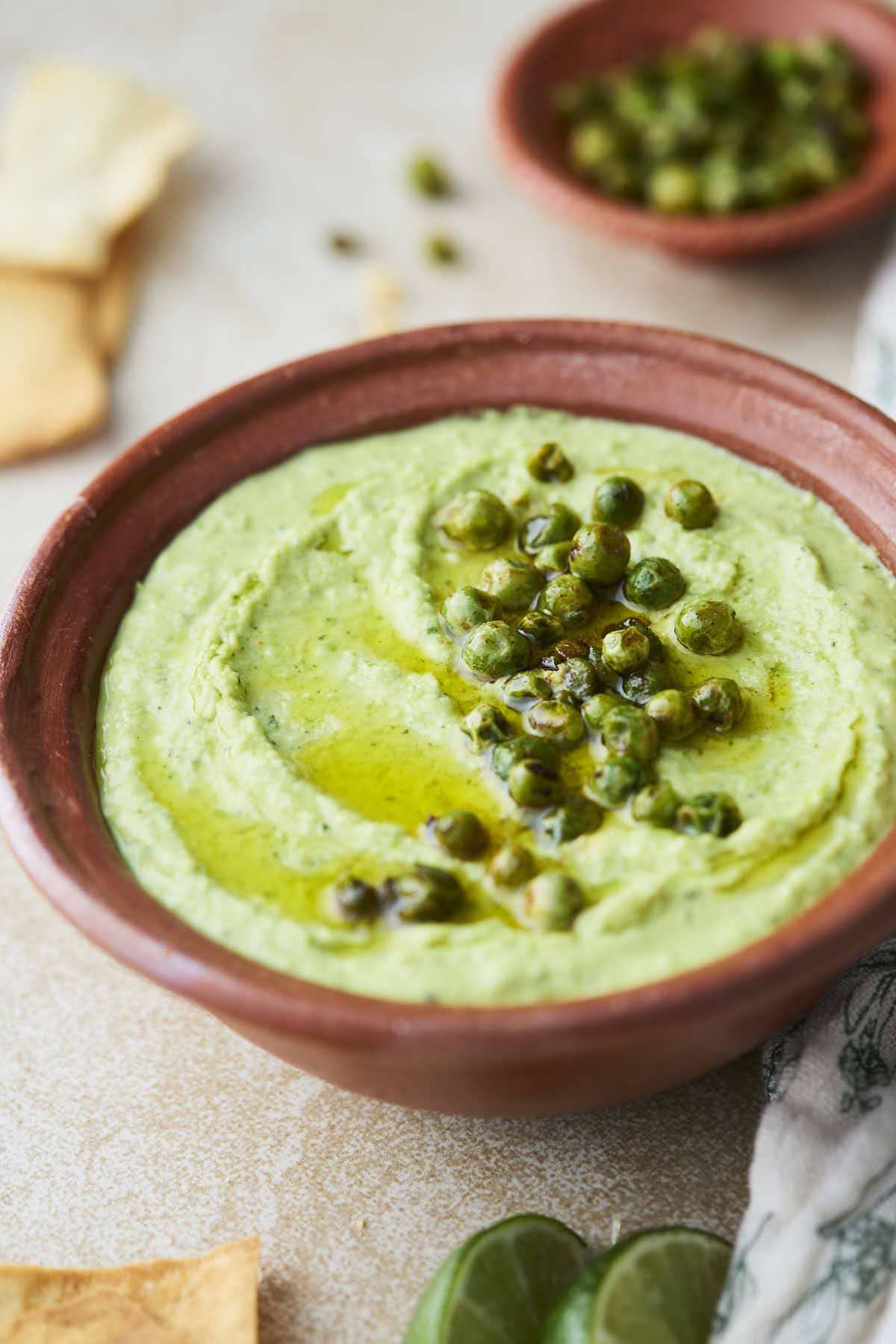 Green pea hummus in a terracotta bowl, topped with roasted green peas and a drizzle of olive oil.