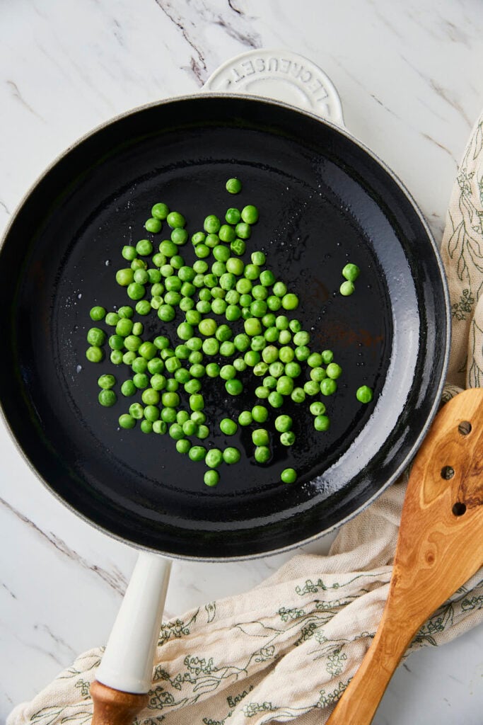 Raw green peas in a frying pan before roasting.