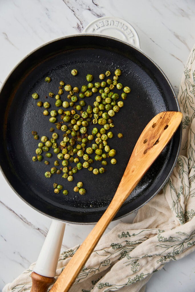 Roasted green peas in a frying pan with wooden spatula after roasting.