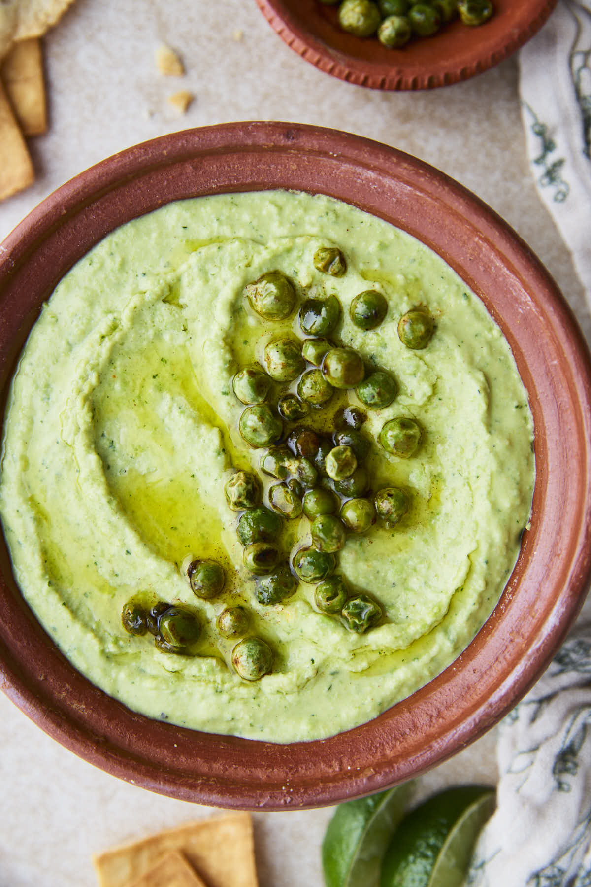 A bowl of creamy green peas hummus garnished with roasted green peas and a drizzle of olive oil.