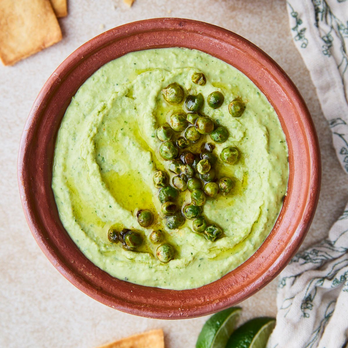 A bowl of creamy green peas hummus garnished with roasted green peas and a drizzle of olive oil.