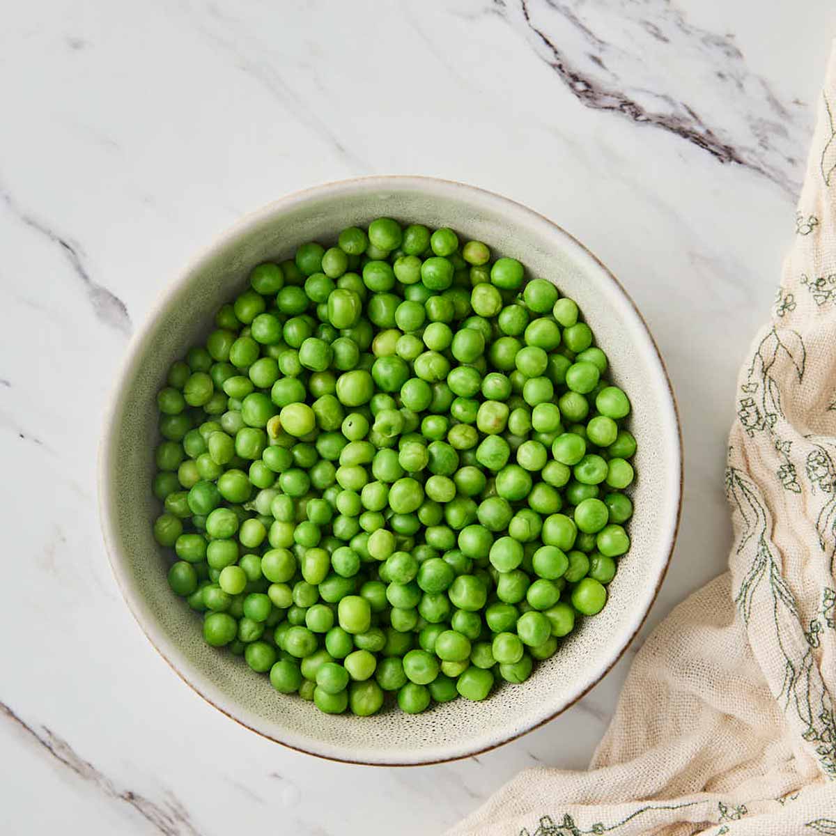 Cooked green peas in a ceramic bowl with water after cooking in microwave