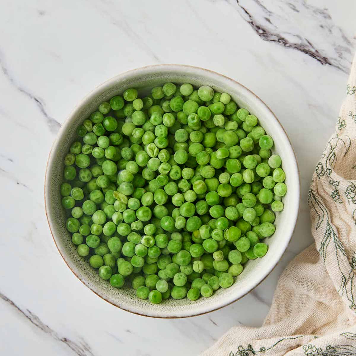 Raw green peas in a ceramic bowl with water before cooking them in microwave