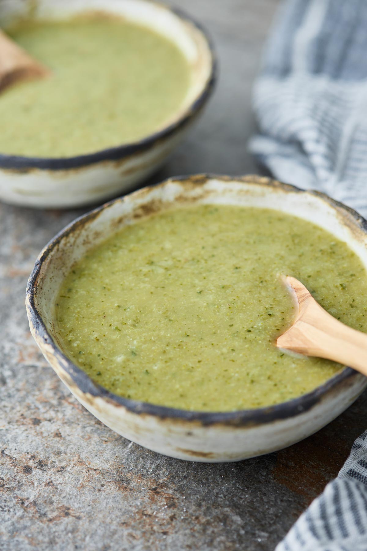 Blended zucchini soup in a serving ceramic bowl with a wooden spoon.