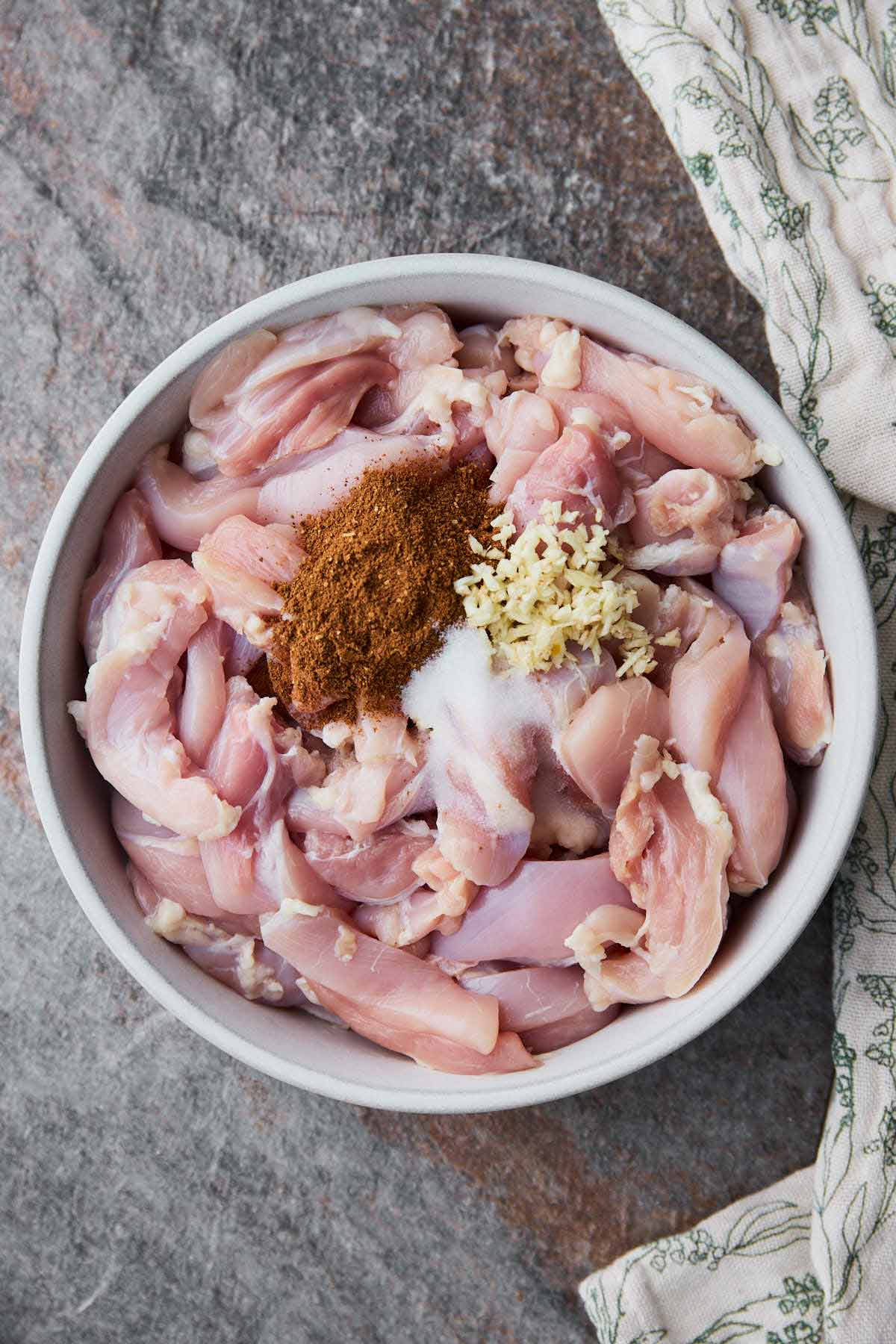 Sliced raw chicken with shawarma spice mix, salt and garlic in a mixing bowl ready for marination.