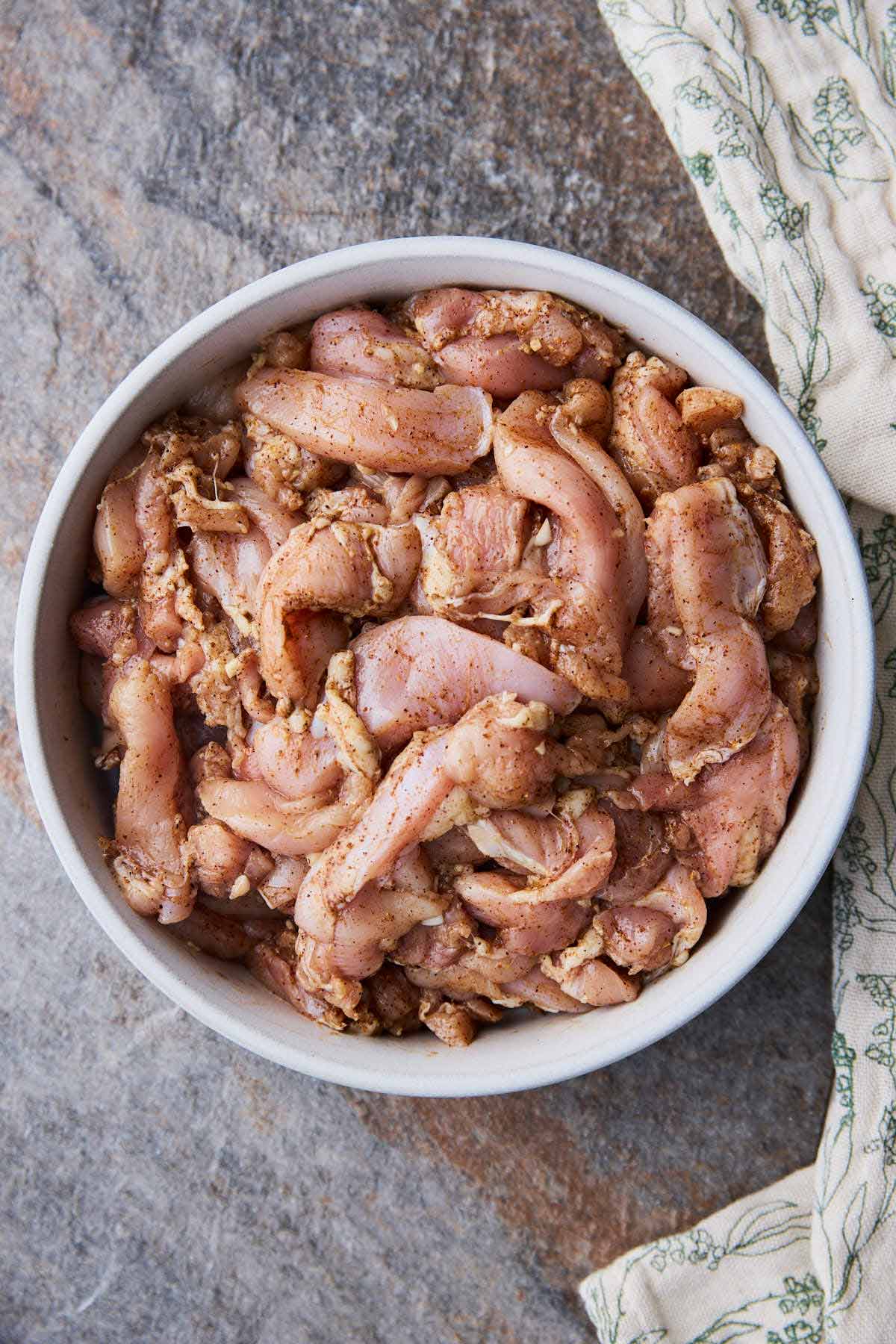 Raw chicken marinated with shawarma spices in a mixing bowl.