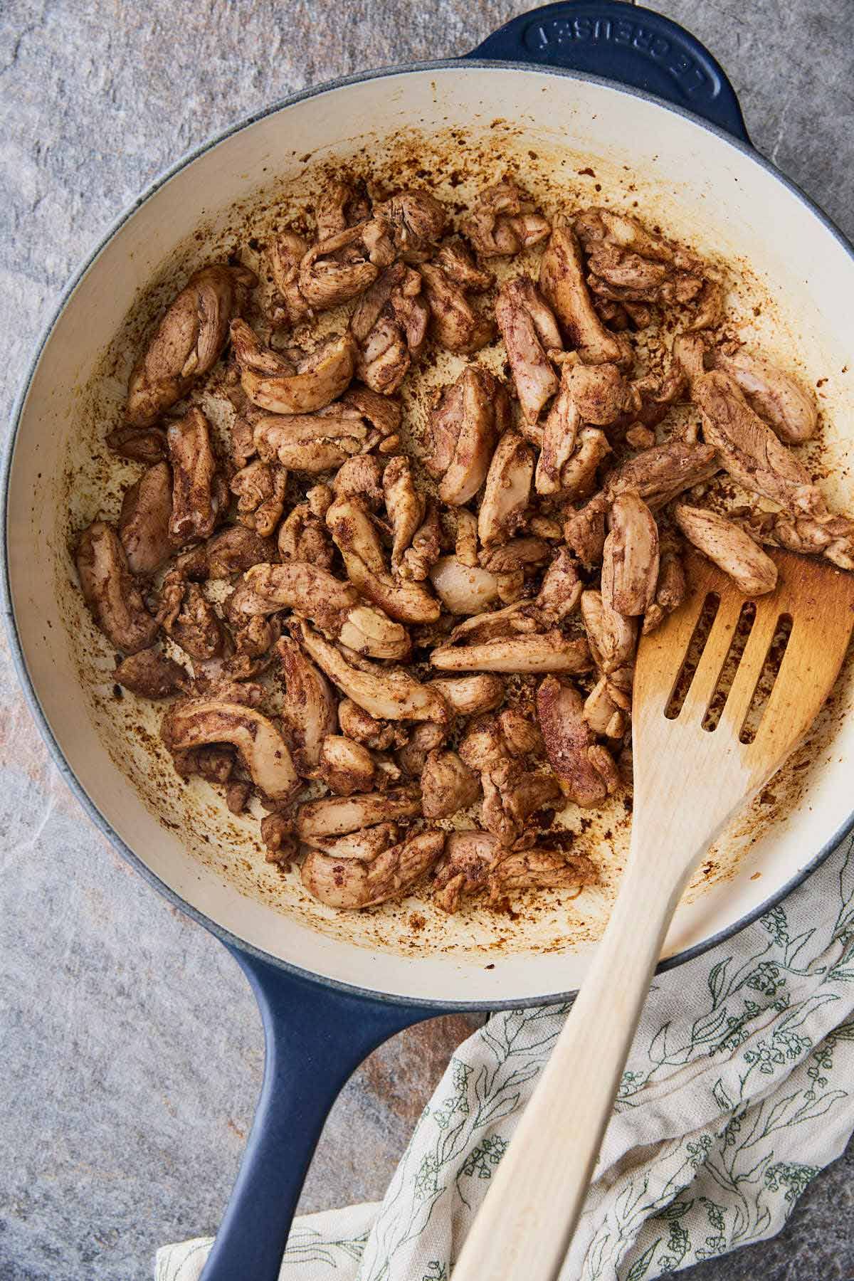 Roasted shawarma chicken in a skillet with wooden spatula.