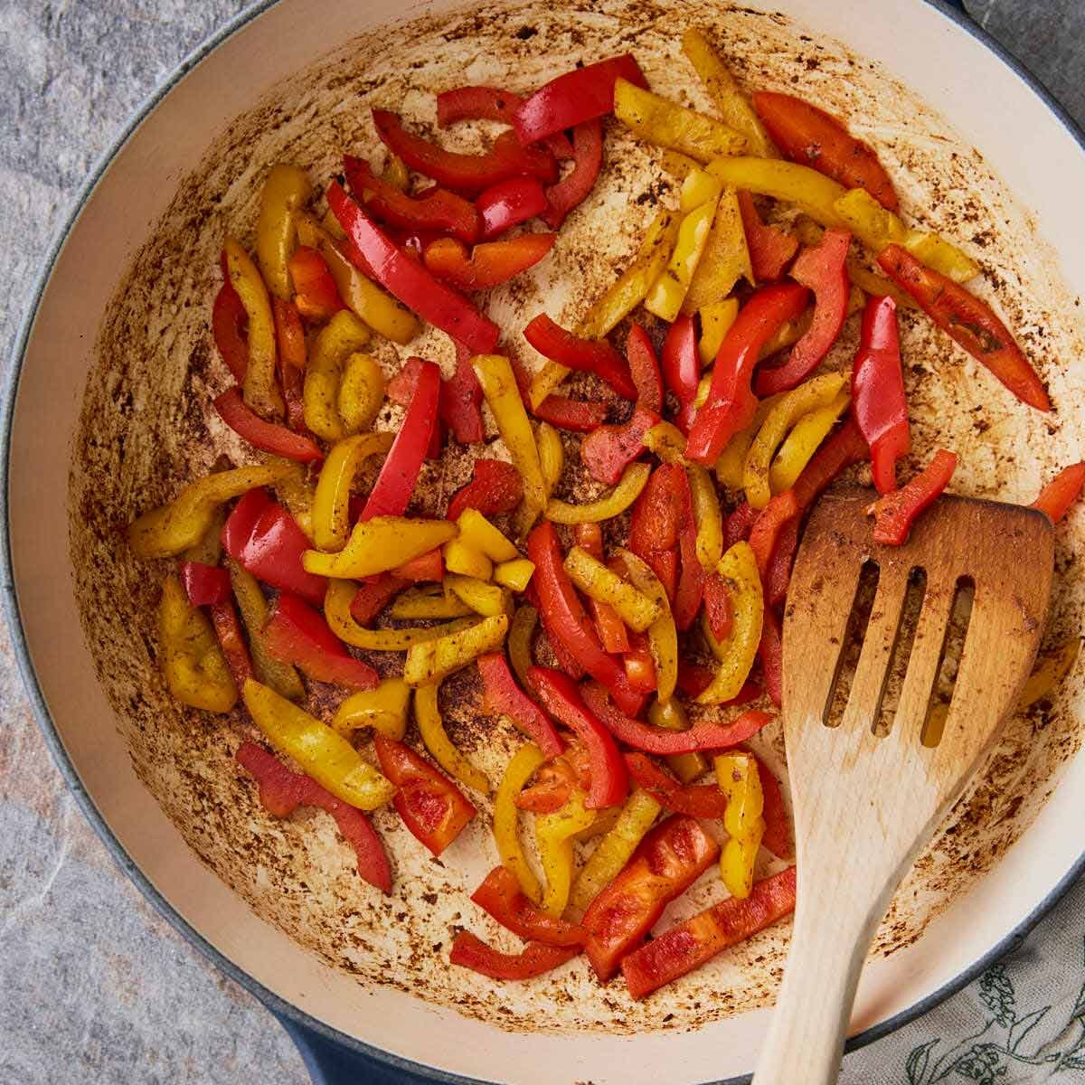 Roasted red peppers in a skillet with wooden spatula.
