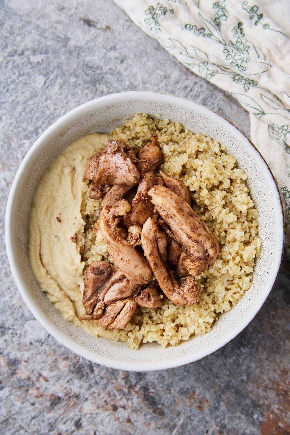 A bowl with creamy hummus shawarma chicken and fluffy quinoa