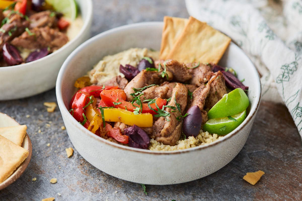 Shawarma chicken hummus bowl - a bowl filled with shawarma chicken, creamy hummus, fluffy quinoa, and roasted peppers, topped with fresh cilantro, olives and lime for garnish.






