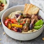 A bowl filled with shawarma chicken, creamy hummus, fluffy quinoa, and roasted peppers, topped with fresh cilantro, olives and lime for garnish.
