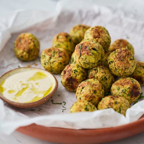 Zucchini meatballs with a dipping sauce on the side, served on a terracotta plate lined with parchment paper.