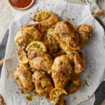Baked lemon pepper chicken drumsticks with lemon slices on a serving platter.