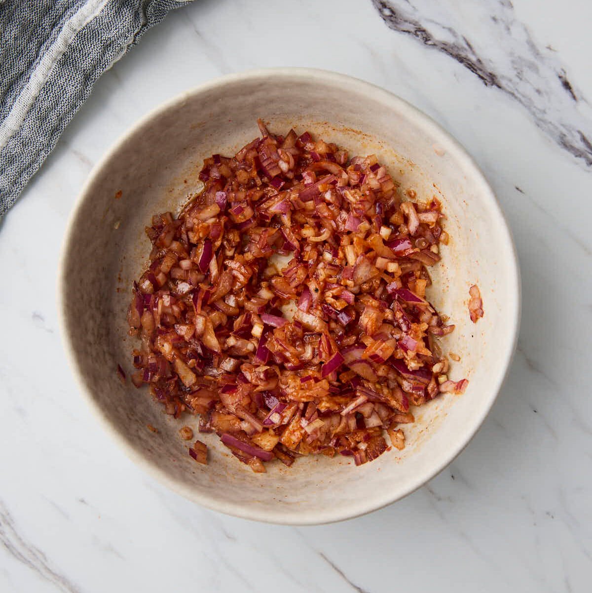 Chopped red onion and spice mixture mixed together in a bowl.