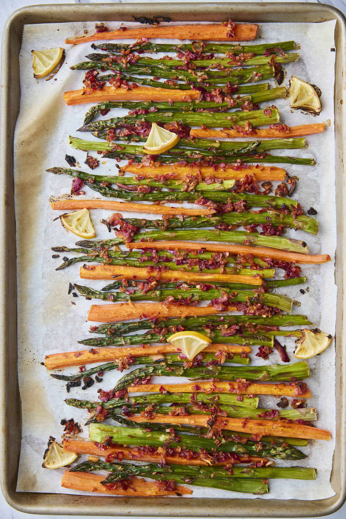 Roasted asparagus and carrots fresh from the oven, lightly browned with caramelized onions and lemon wedges scattered on top.